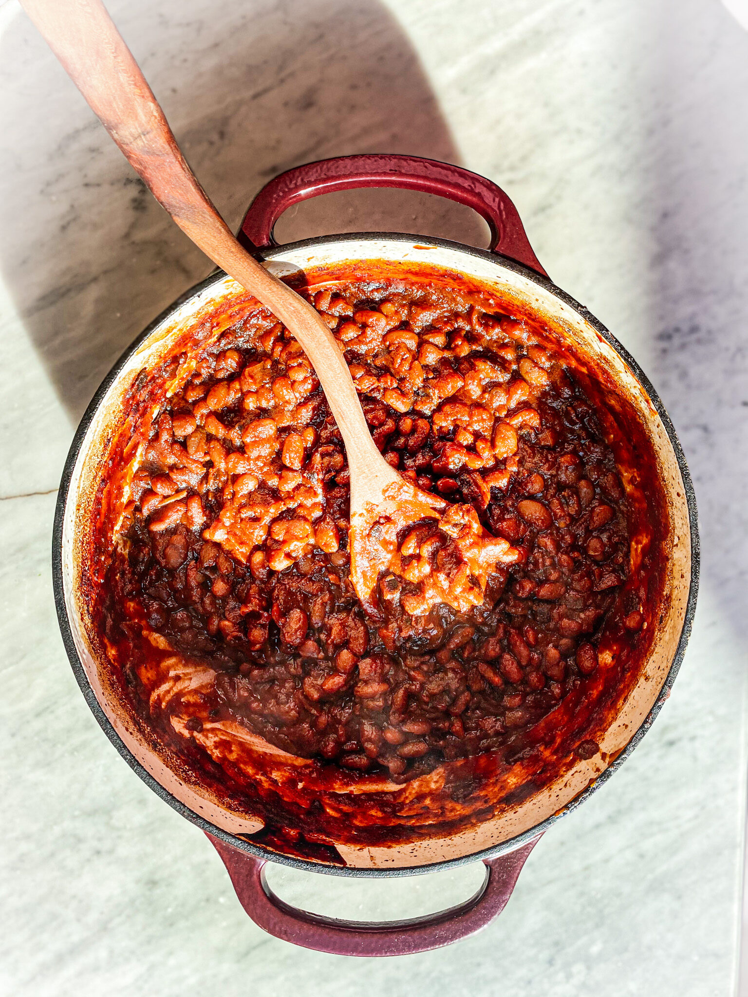 Baked beans in a cast iron dutch oven with a wooden spoon