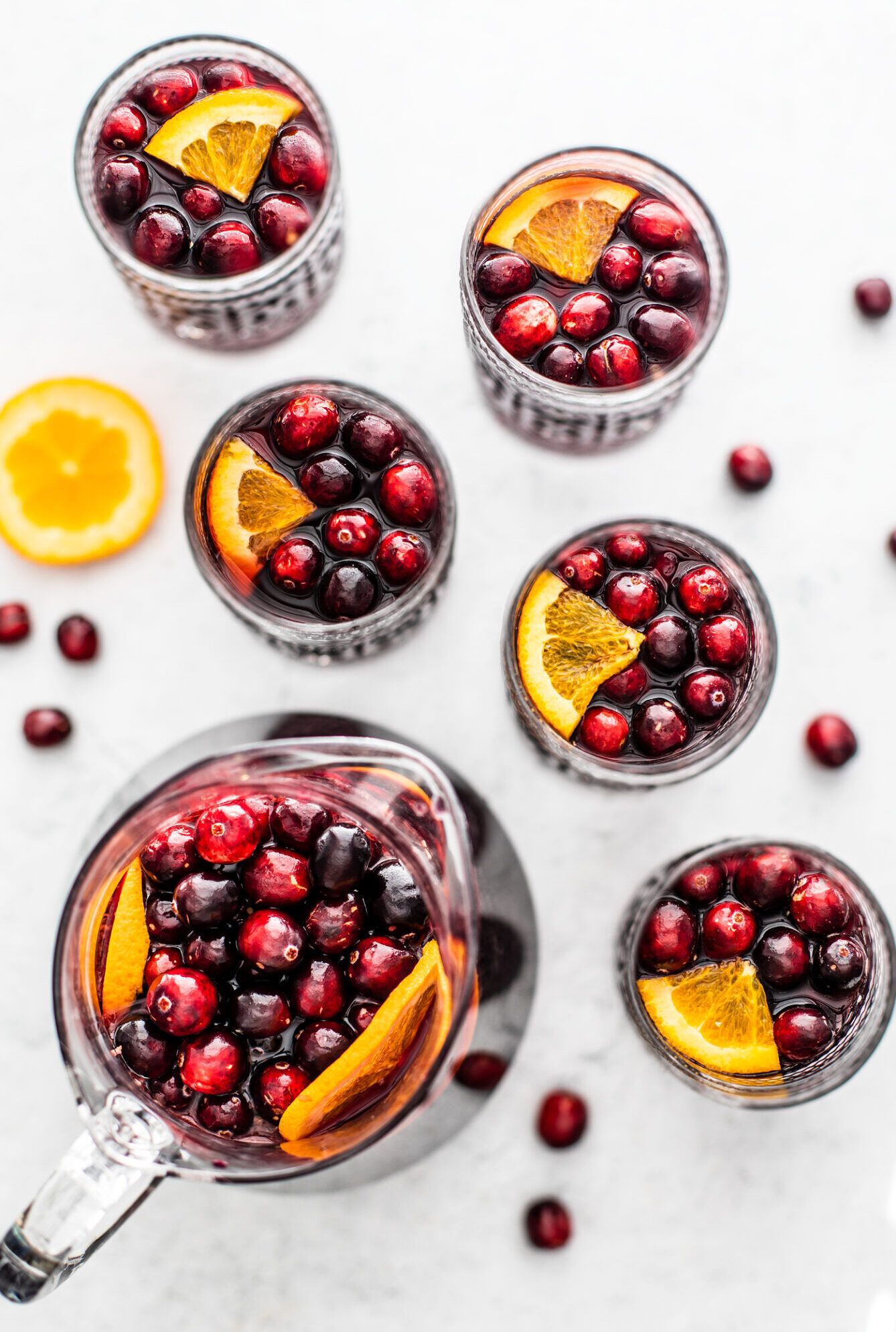 cranberry orange red sangria in a pitcher and glasses with cranberries and oranges