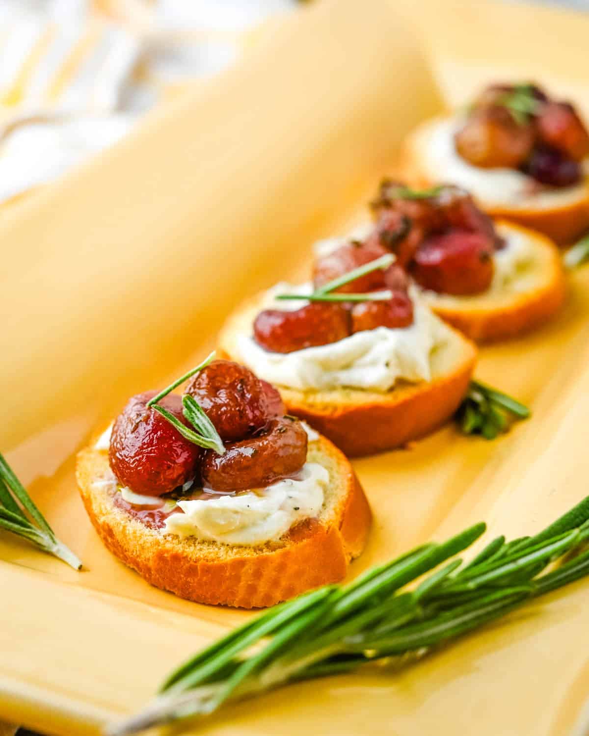 grape and goat cheese crostini on a tray with rosemary branch