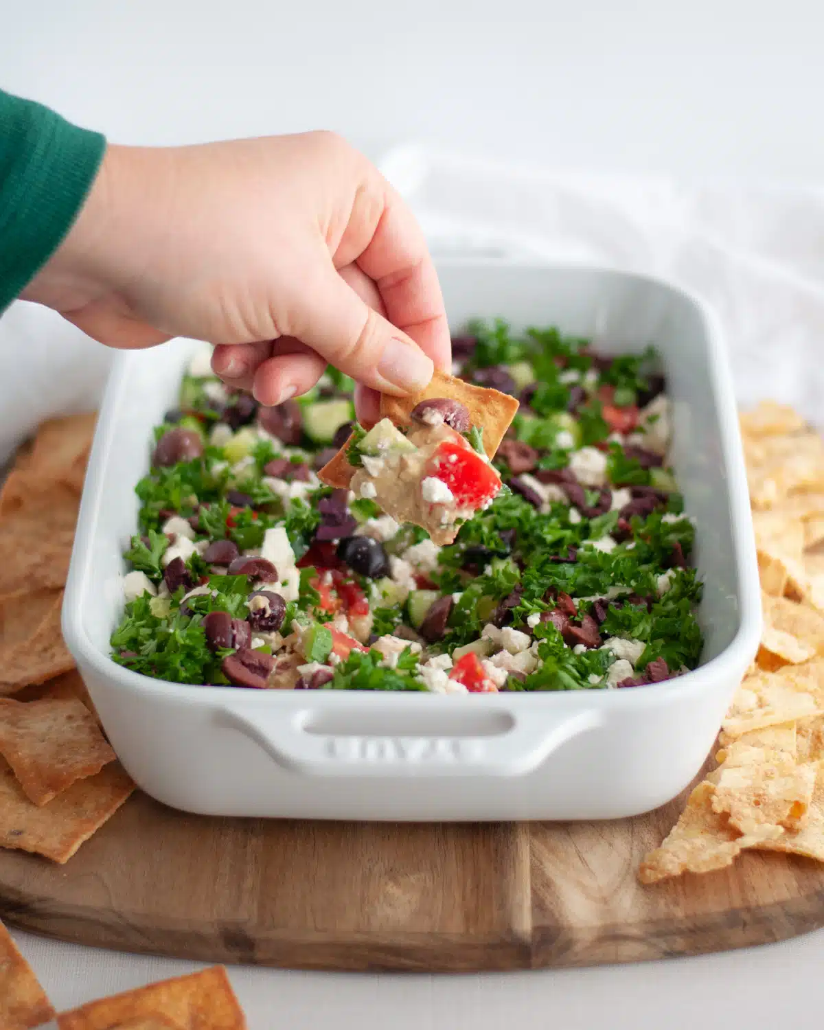 Greek layered dip with a hand dipping out of the pan