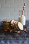 Pecan sandies stacked to the side with pecans and a glass of milk and a red and white straw