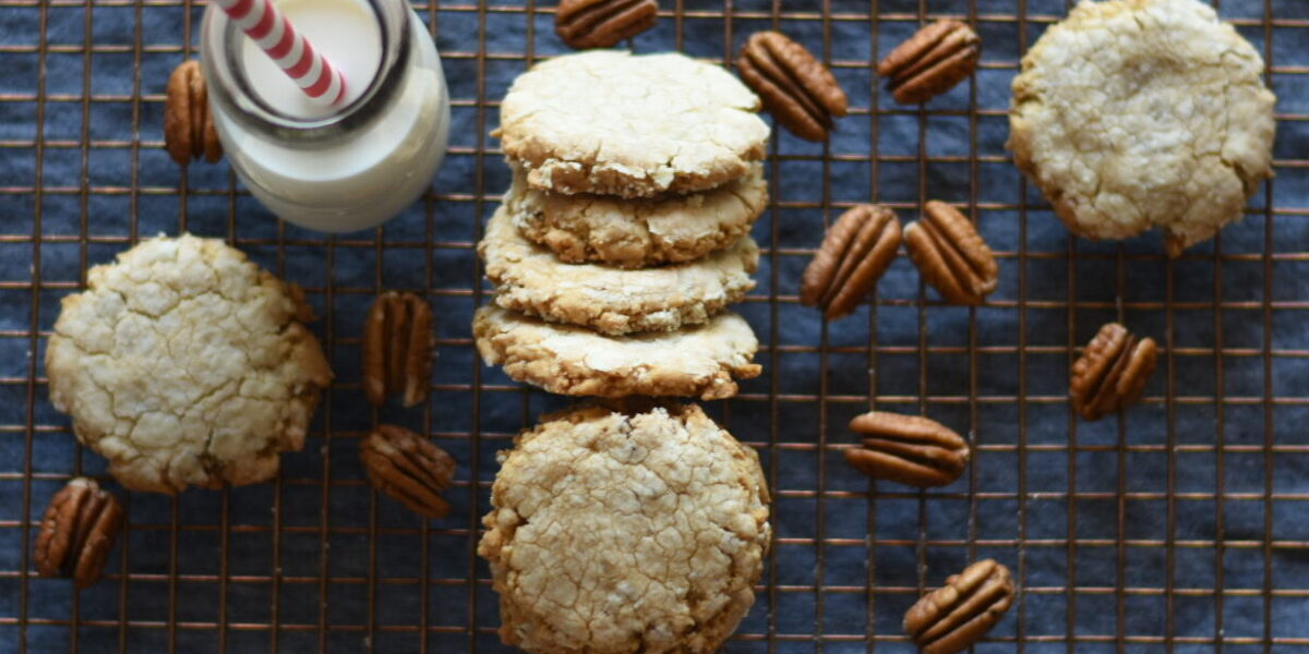 Pecan sandies and pecans and a milk glass with a red and white straw
