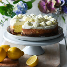lemon cheese cake with a slice out of it and lemons and flowers