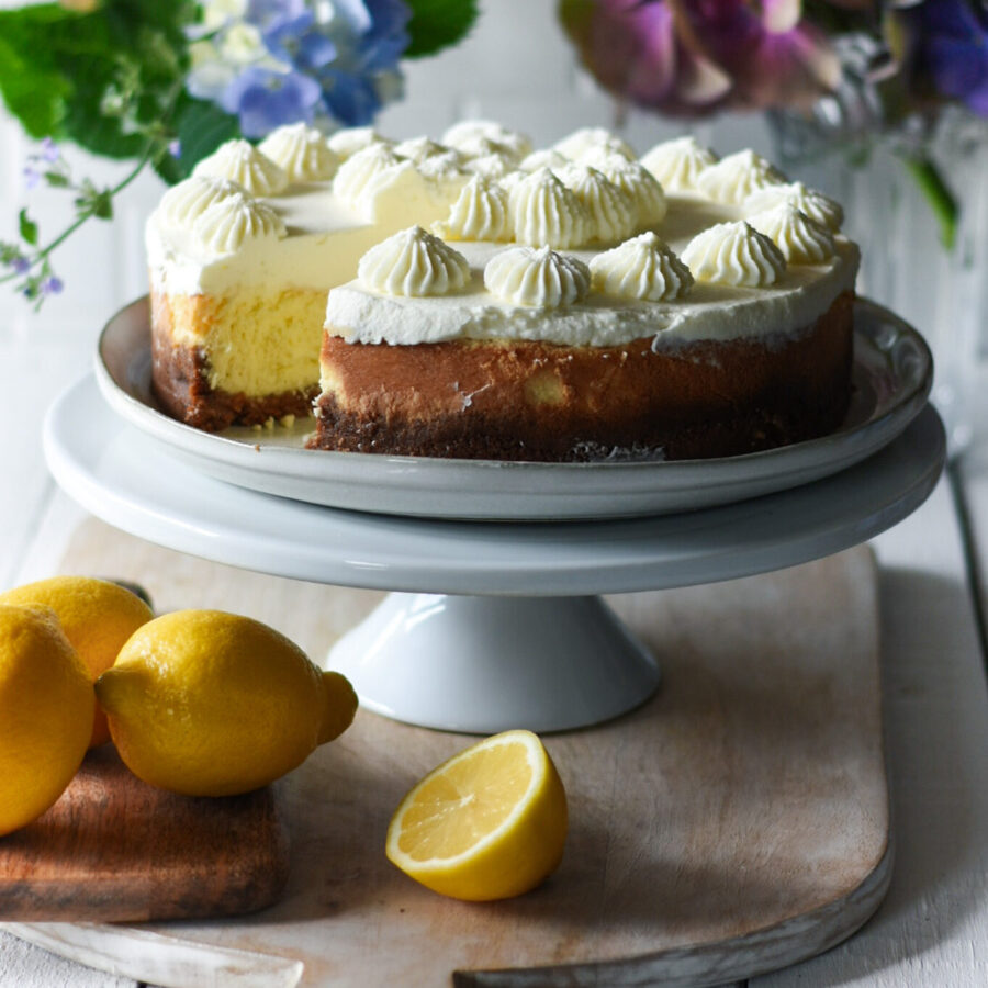 lemon cheese cake with a slice out of it and lemons and flowers