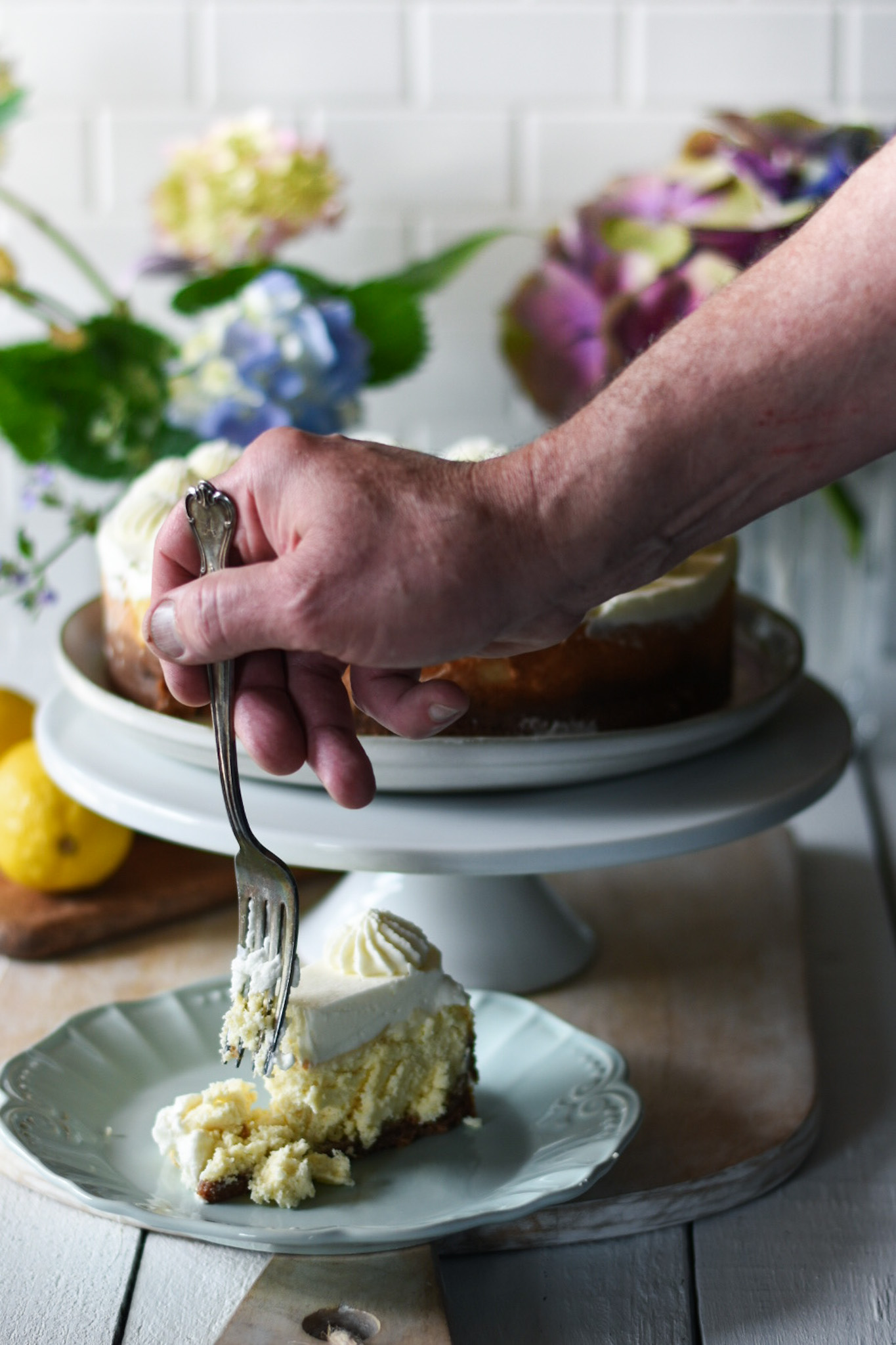 Hand with fork eating a piece of lemon cheesecake with lemon cheesecake and flowers