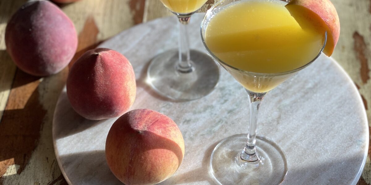 peach martinis on a marble round with peaches