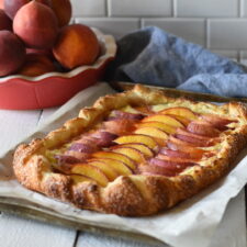 Cream cheese peach galette with a red pie pate of peaches and a blue napkin