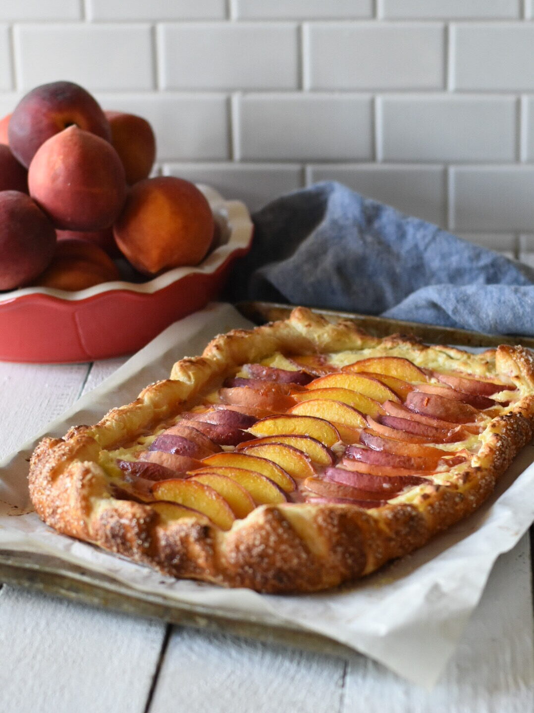 Cream cheese peach galette with a red pie pate of peaches and a blue napkin