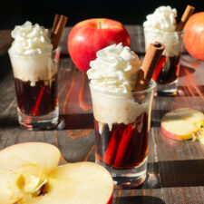 Apple Cinnamon Bourbon shots with whip cream and apples with one sliced