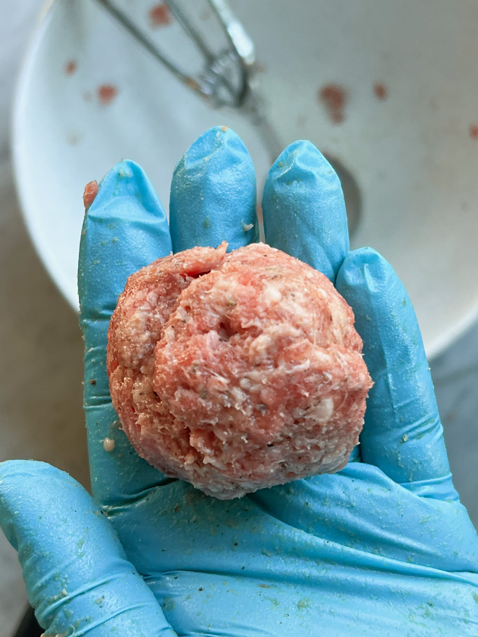 ground beef and breakfast sausage meatball in a hand with a rubber glove