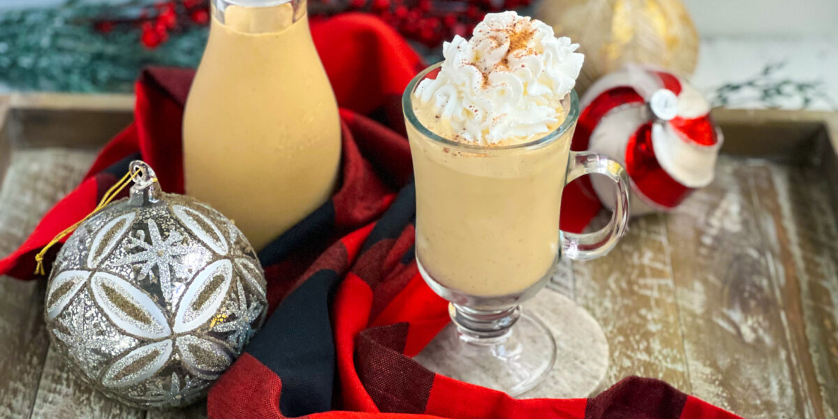 Gingerbread eggnog with whipped cream and nutmeg in a glass with ornaments and a black and red napkin