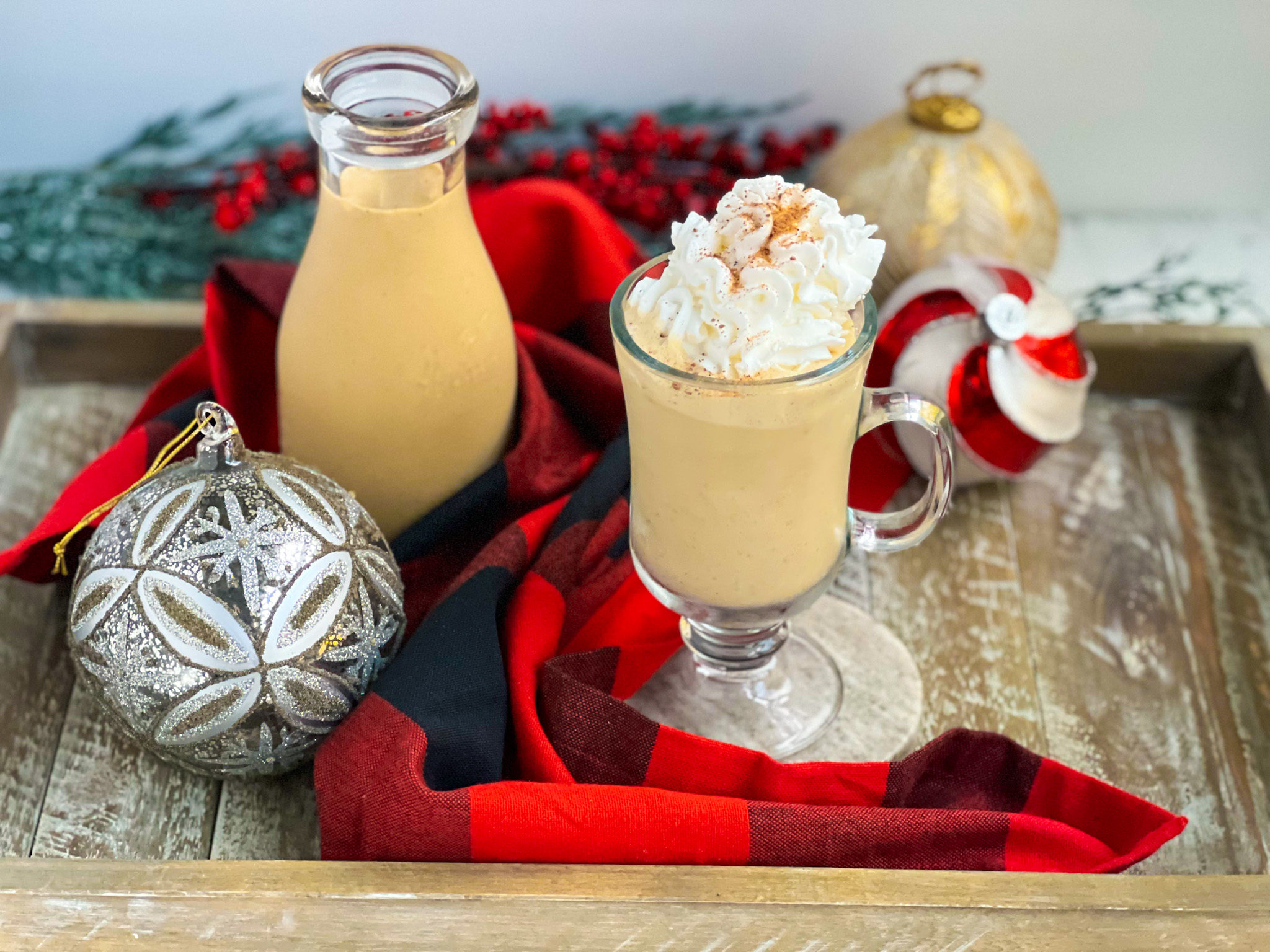 Gingerbread eggnog with whipped cream and nutmeg in a glass with ornaments and a black and red napkin