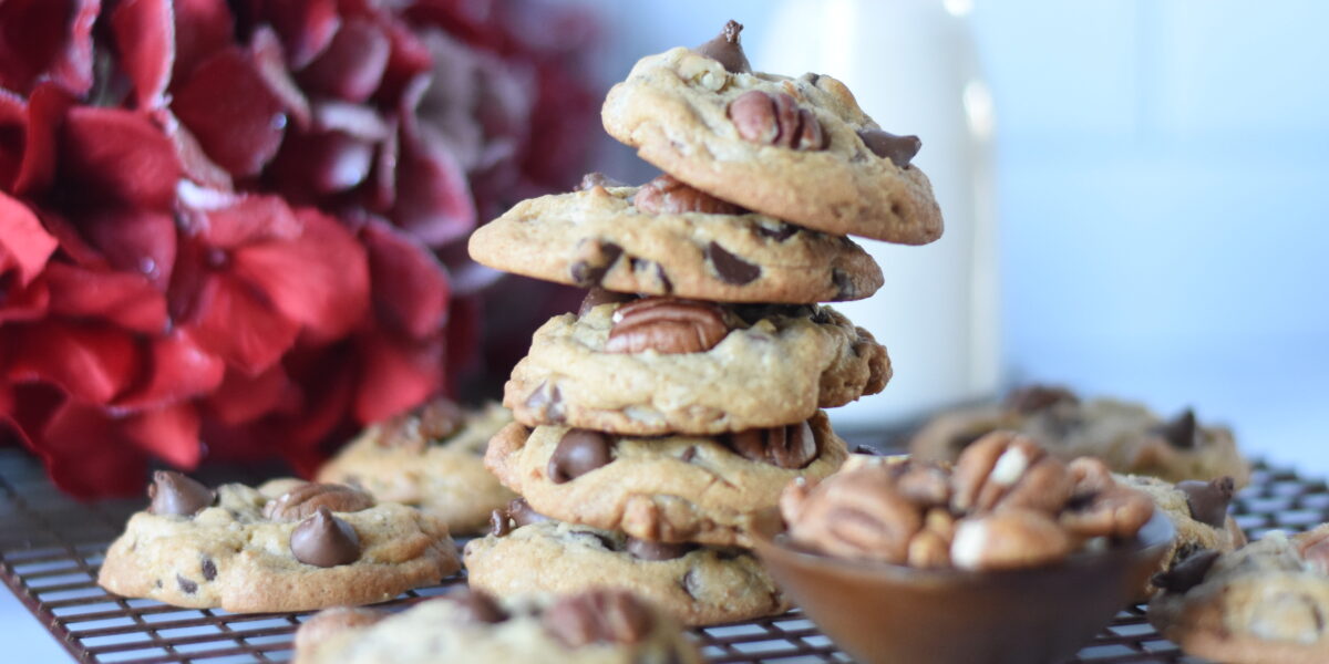 Chocolate chip pecan cookies stacked with a bottle of milk and a straw ad a bowl of pecans