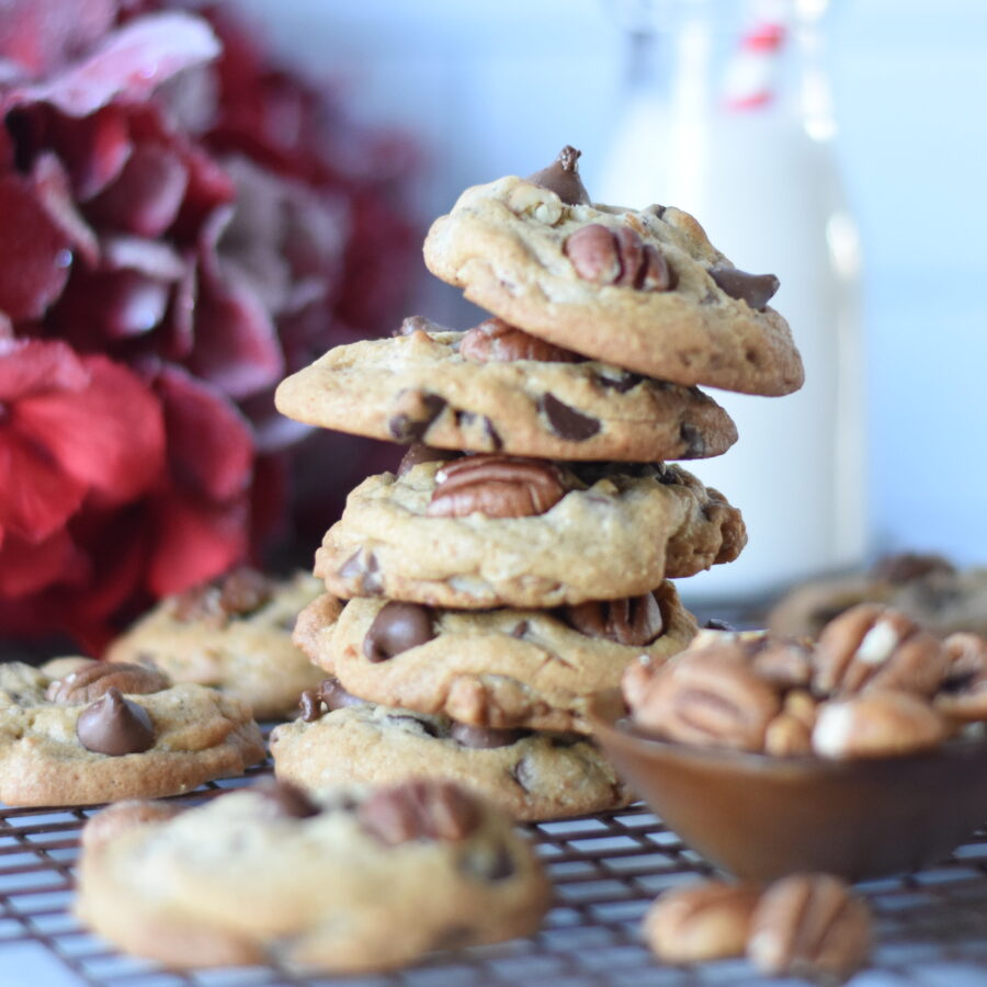 Chocolate chip pecan cookies stacked with a bottle of milk and a straw ad a bowl of pecans
