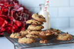 stack of pecan chocolate chip cookies with milk and a straw and red flowers