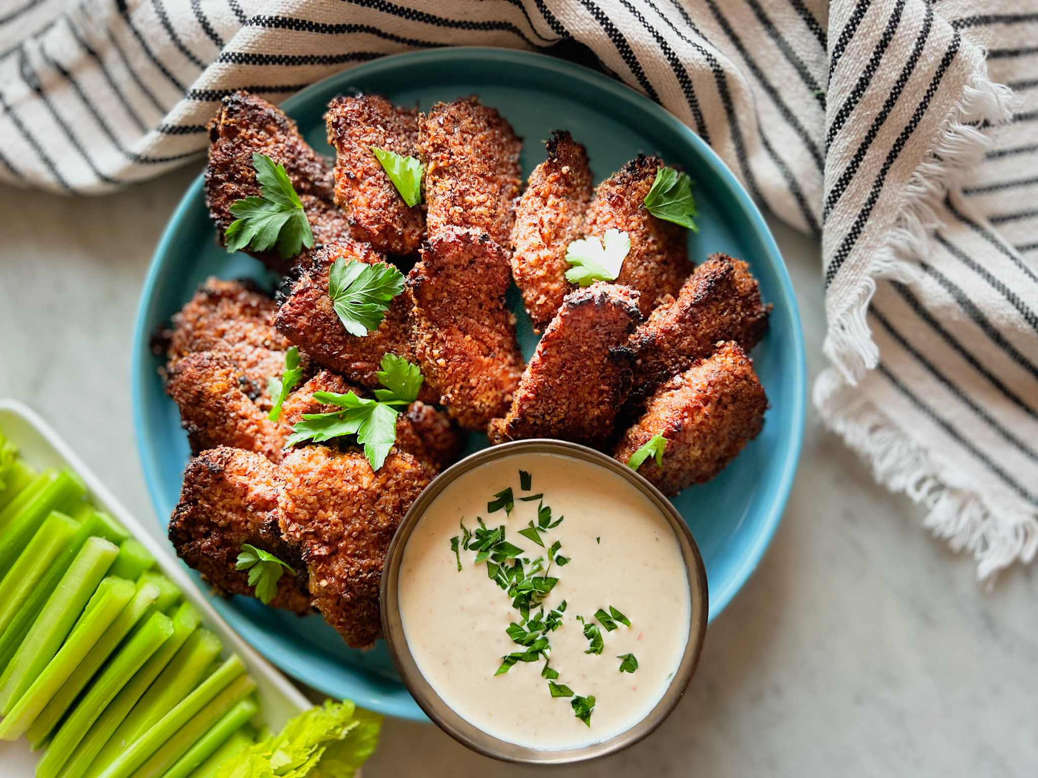 Gluten free pecan crusted chicken tenders on a blue plate with a peach dipping sauce, celery and a striped napkin