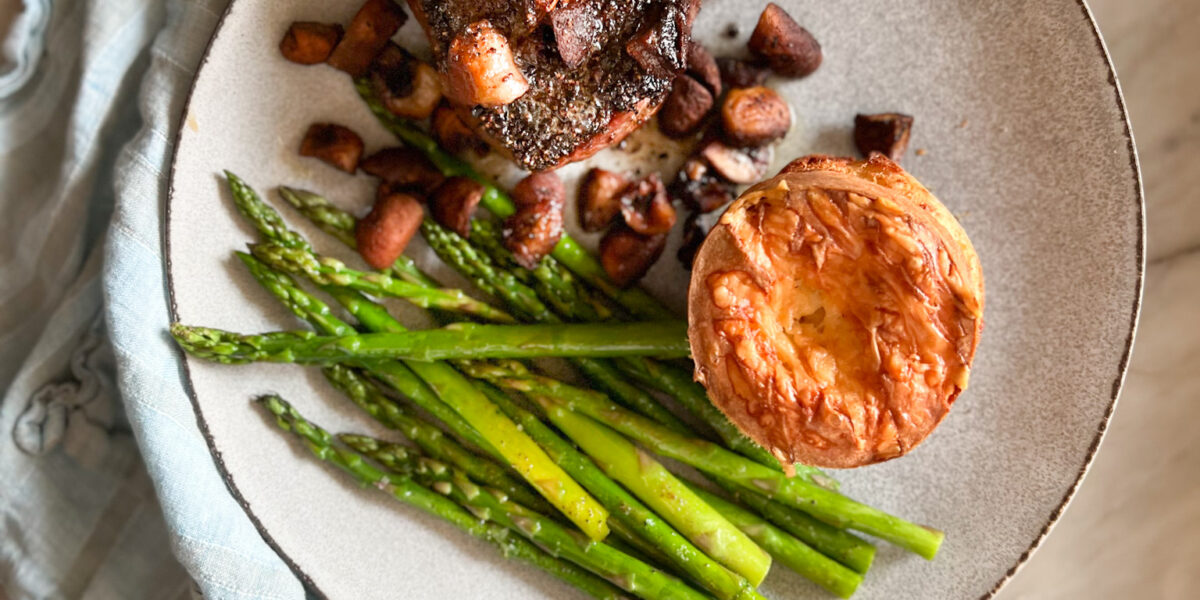 steak and mushrooms and asparagus and cheese popover on a plate with a blue napkin