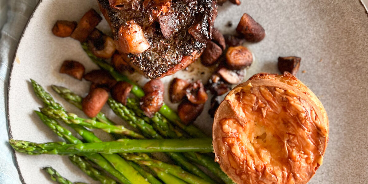 steak and mushrooms and asparagus and cheese popover on a plate with a blue napkin