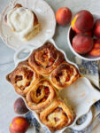peach cobbler rolls baked with one frosted and a bowl of peaches