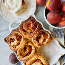 peach cobbler rolls baked with one frosted and a bowl of peaches
