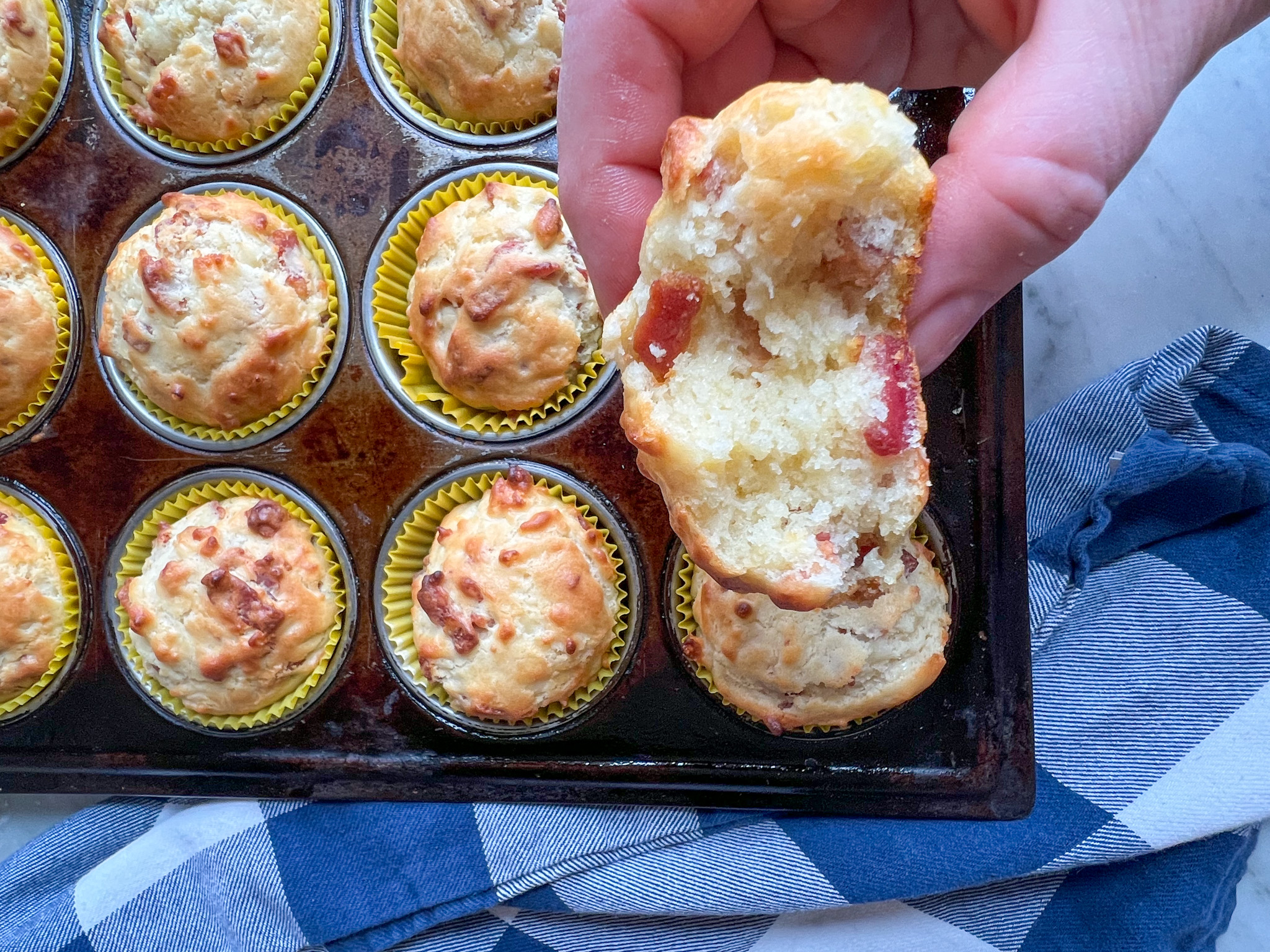 bacon cheese muffins with a blue and white napkin and a hand holding one with a bite out of it