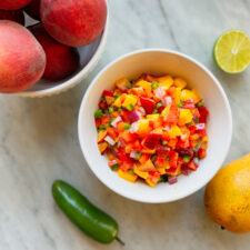 Mango peach salsa in a bowl with a bowl of peaches, jalapeño, mango and lime