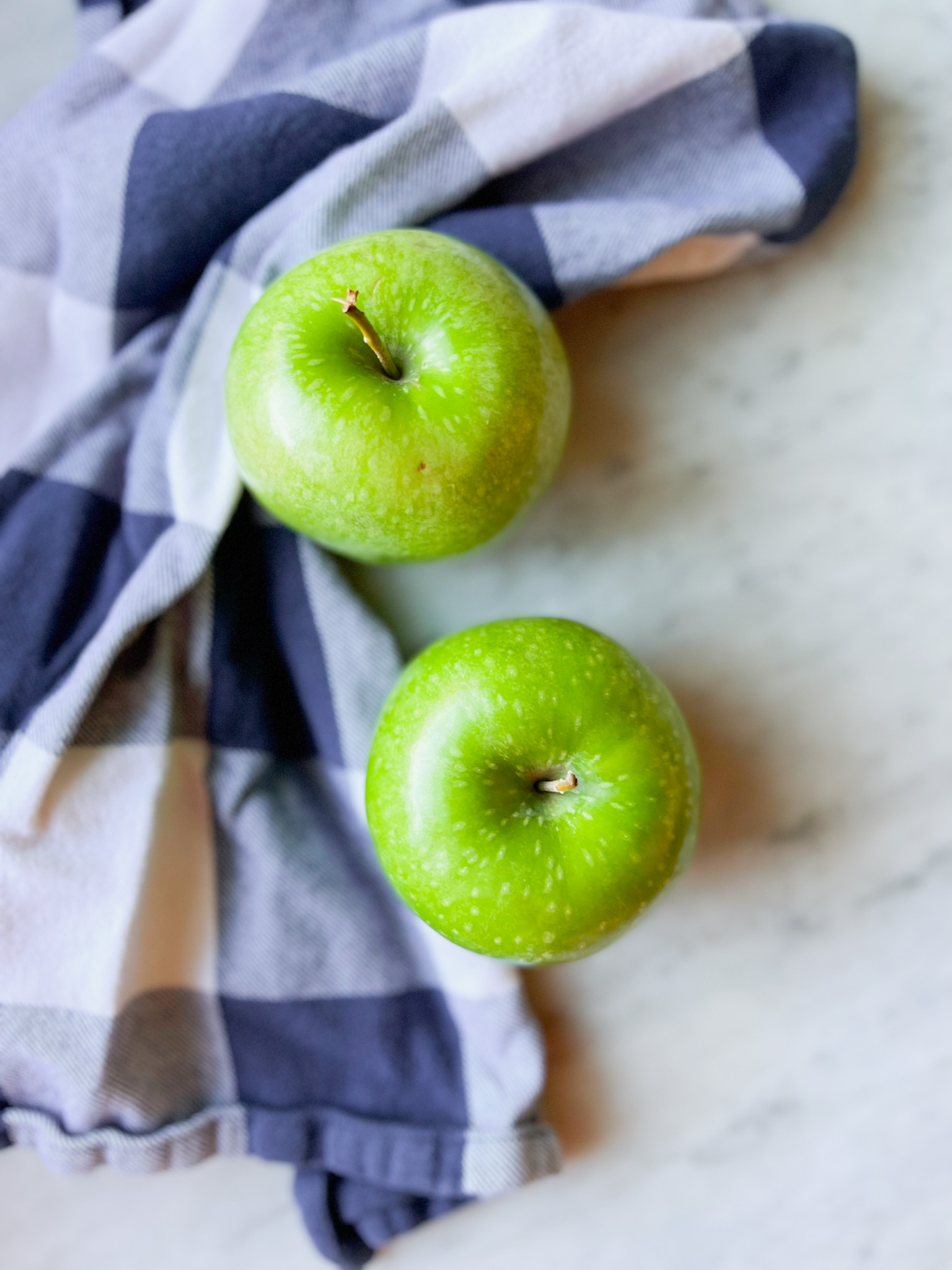2 green granny smith apples with a navy and white napkin