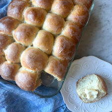 yeast rolls in a pan with one roll on a plate and a blue napkin