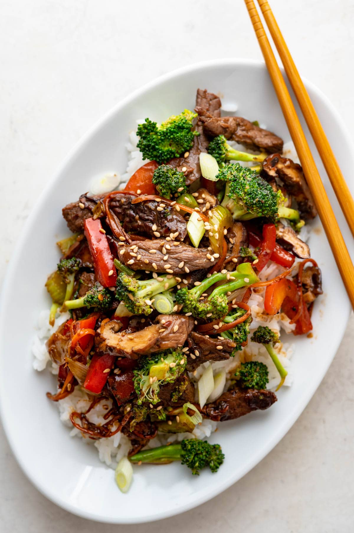Beef and broccoli with red peppers on a platter with chop sticks
