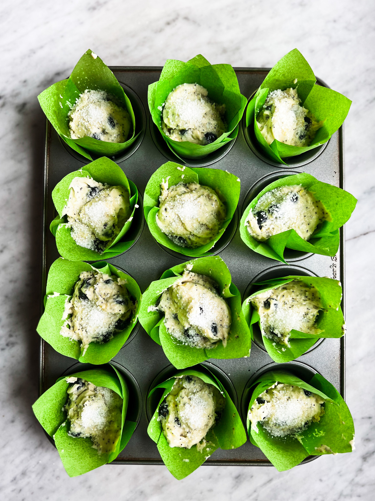 lemon blueberry muffin batter in muffin tins with green muffin liners