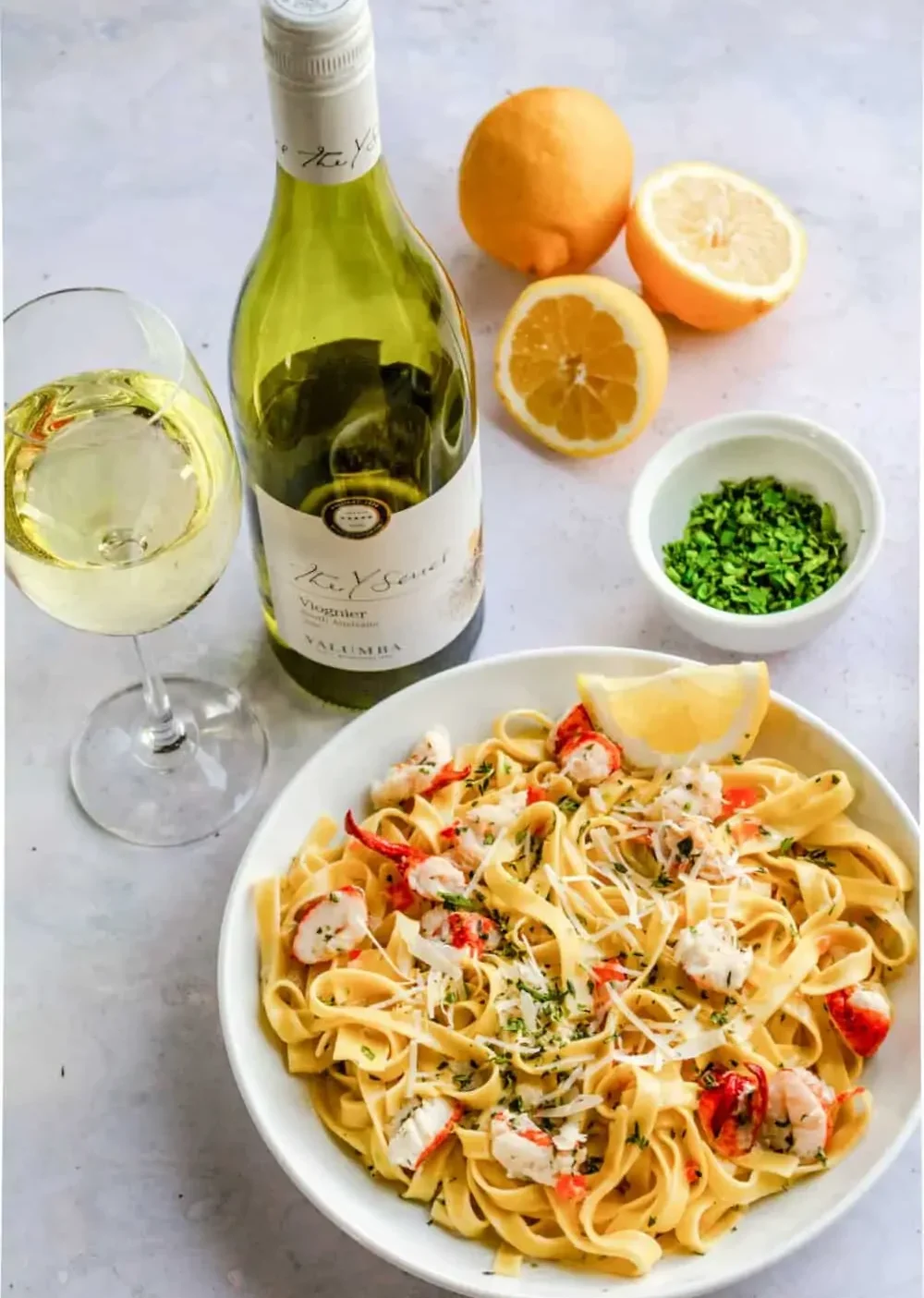lobster pasta with lemons and wine glass and bottle of wine and green herbs