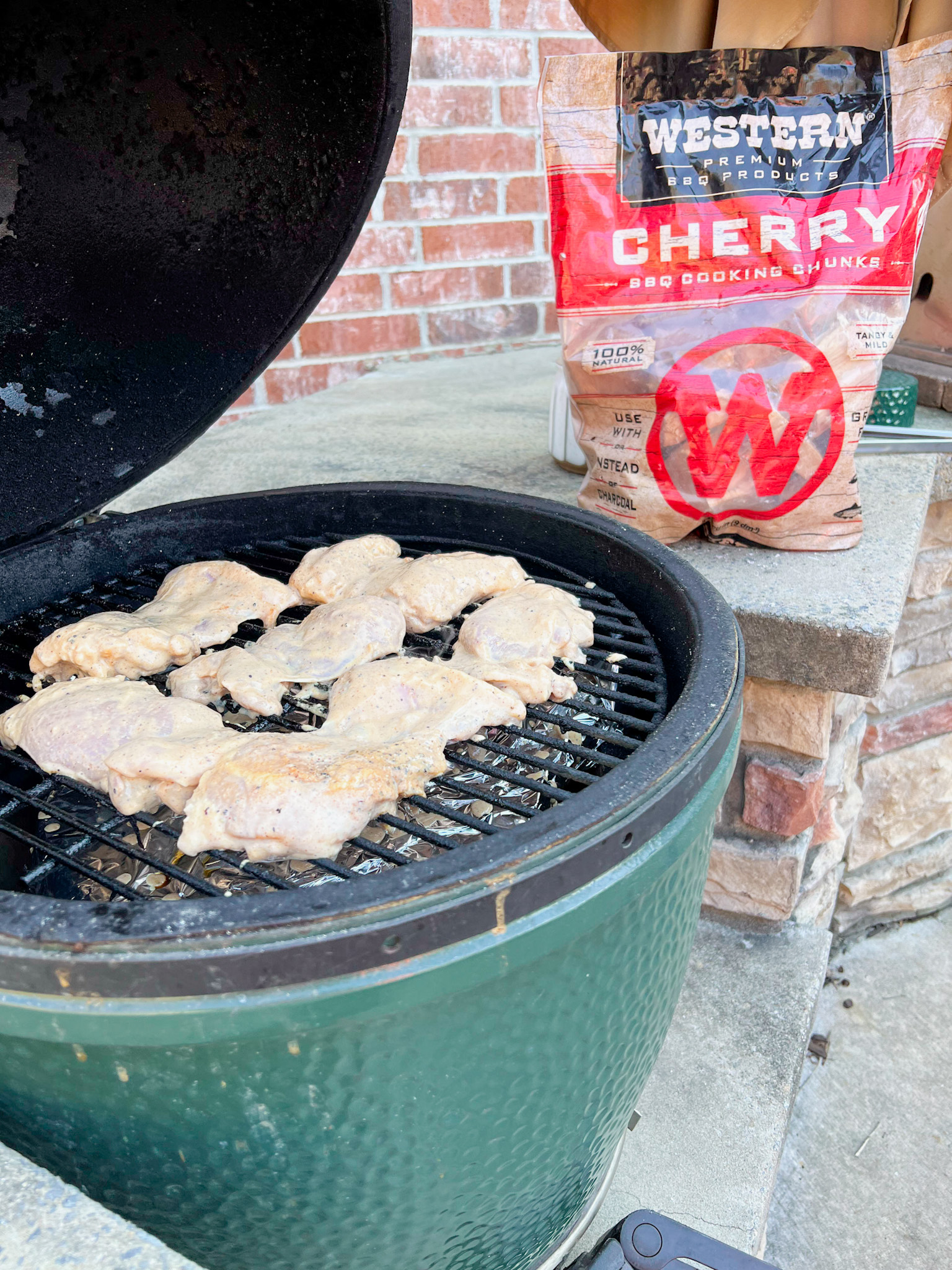 buttermilk marinated chicken thighs on the grill with a bag of western bbq cherry wood chunks