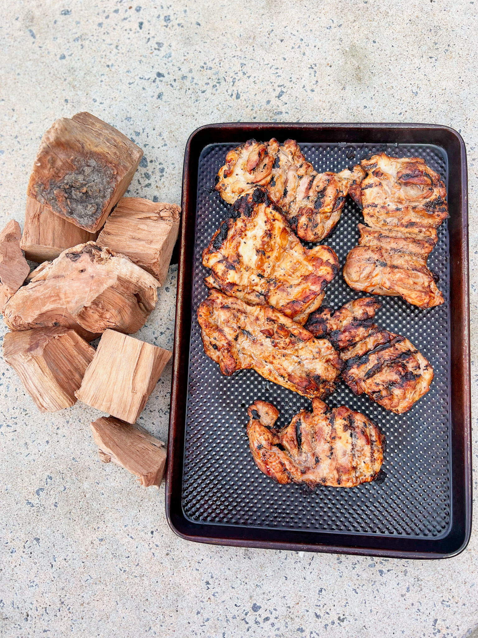 grilled chicken thighs on a tray with cherry wood chunks sitting next to them