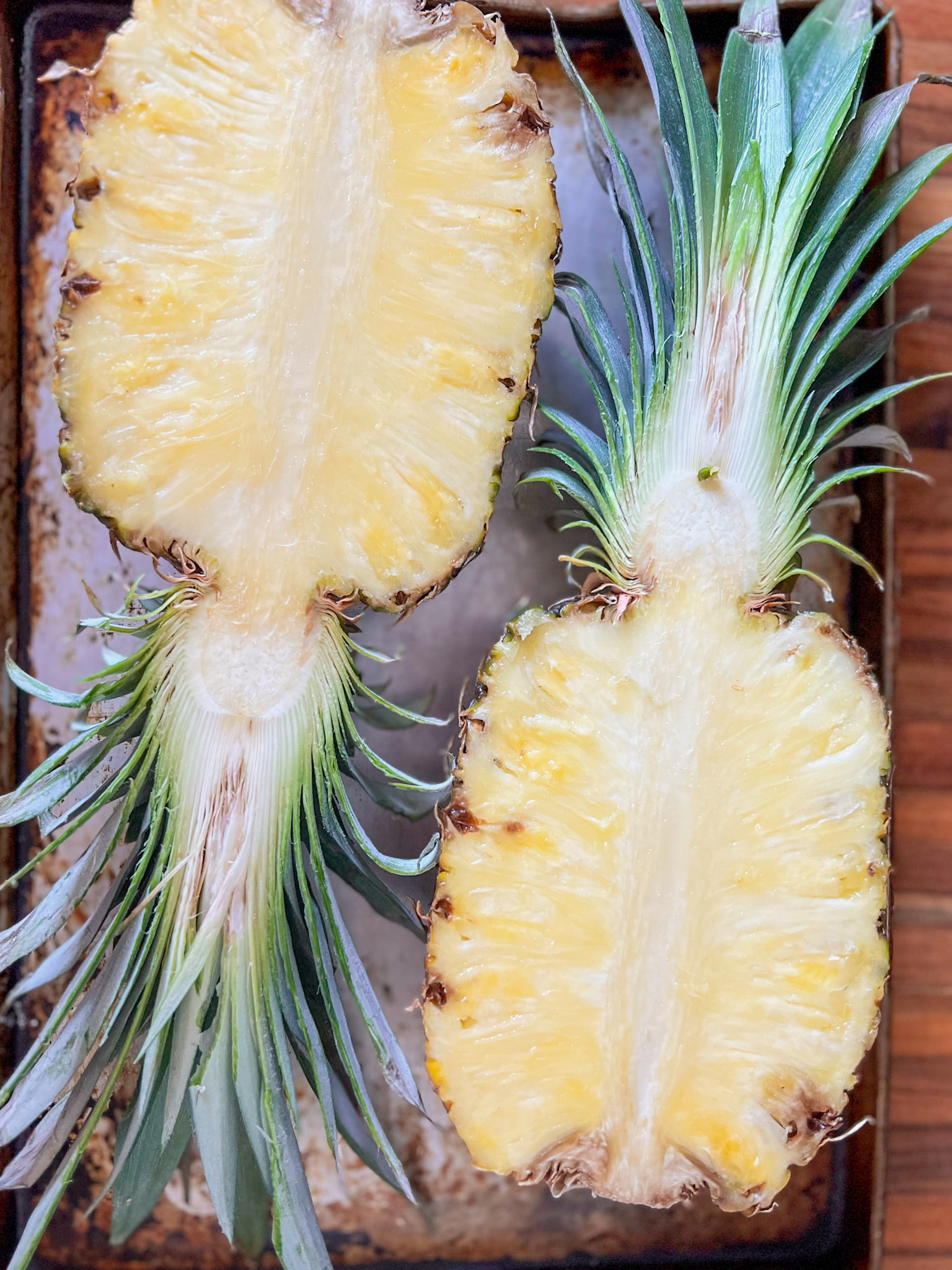 a whole pineapple sliced in half on a cooking sheet