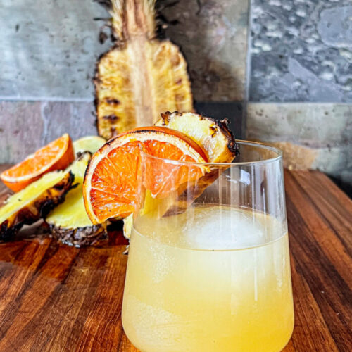 smoked pineapple margarita with a smoked orange slice and smoked pineapple in backround