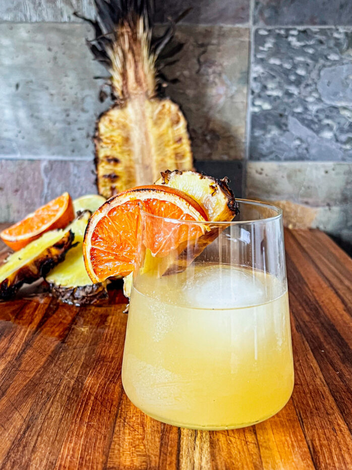 smoked pineapple margarita with a smoked orange slice and smoked pineapple in backround