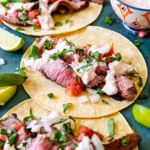 grilled steak tacos laying flat with pico and sauce and limes