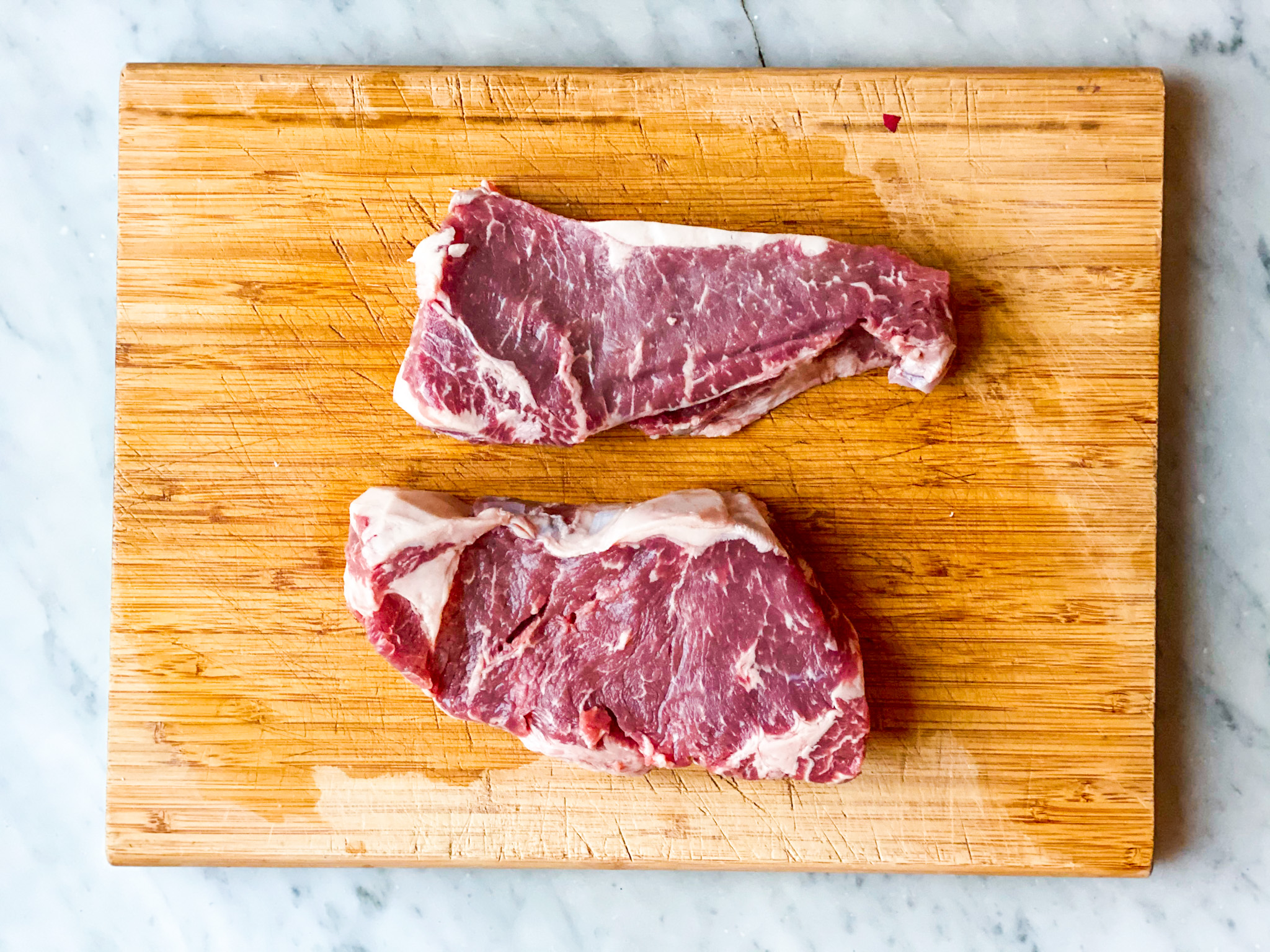 2 raw strip steaks on a cutting board.