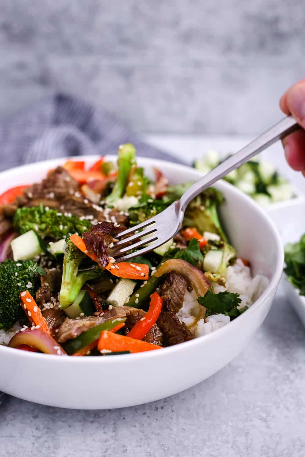 Skirt steak stir fry with veggies in a white bowl with rice and a fork