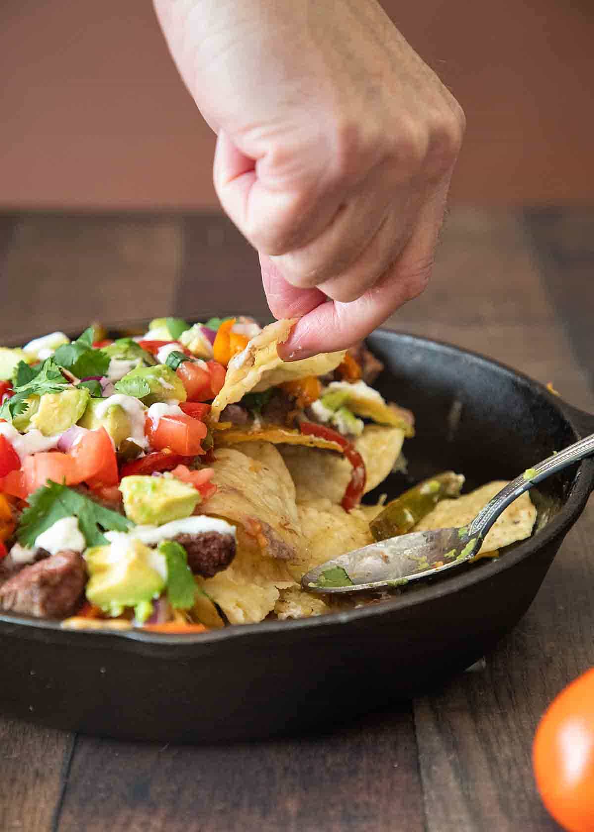 Steak tacos in a pan with a hand grabbing one