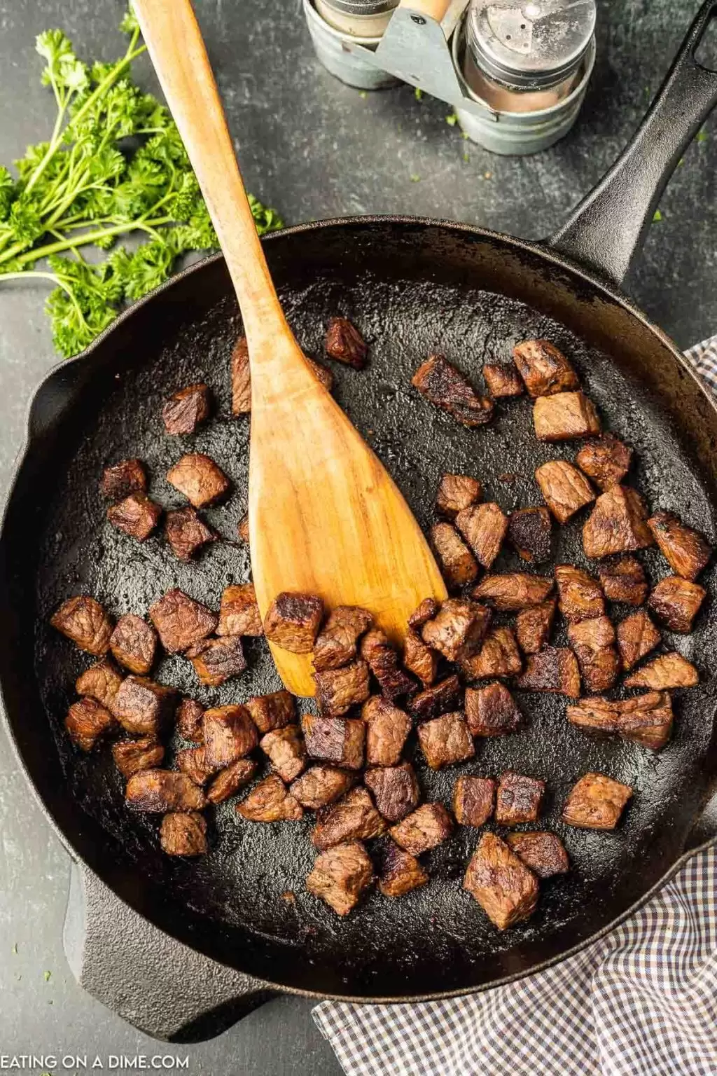 Garlic Butter Steak Bites in a cast iron pan with a wooden spoon and parsley
