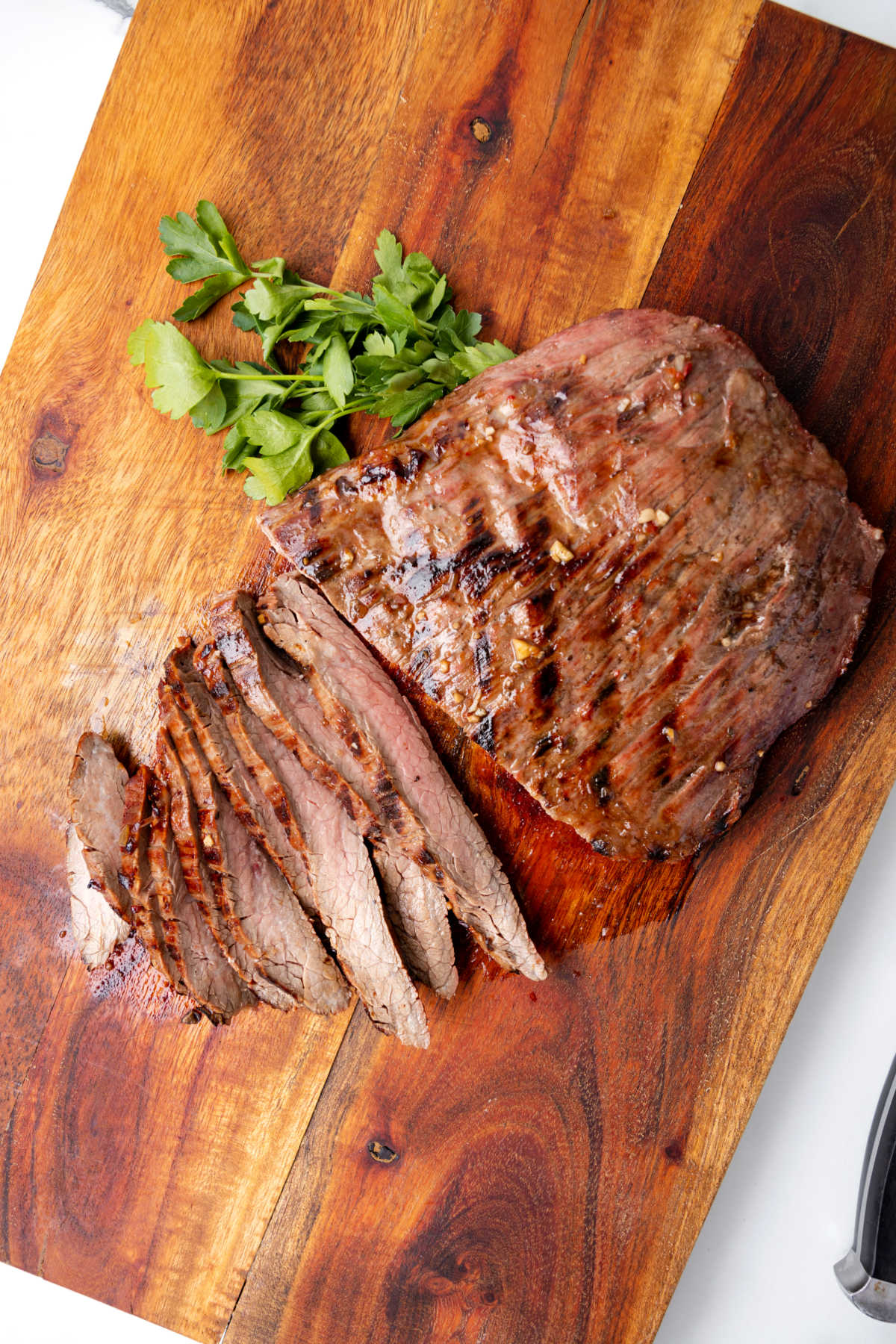 Grilled flank steak sliced on a board with herbs
