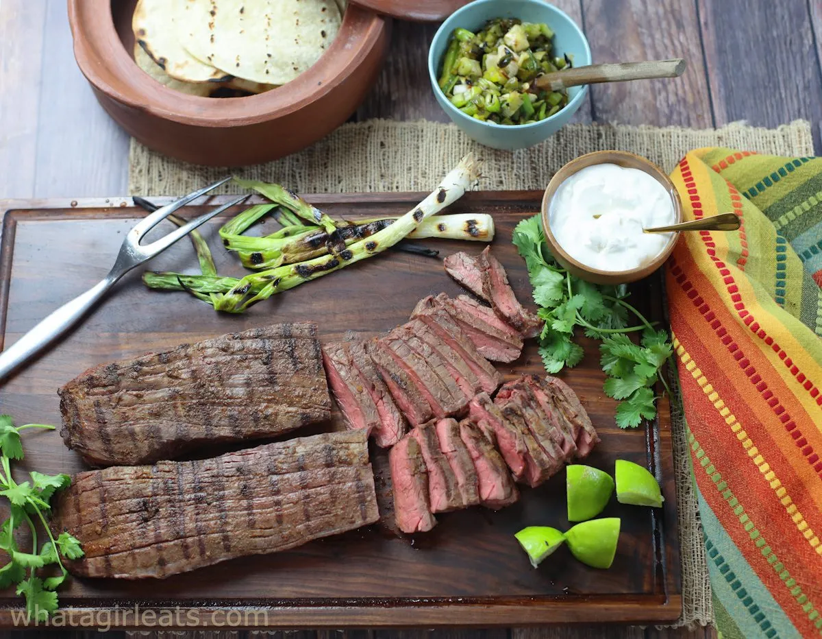 tacos al carbon on a cutting board with limes and green onions and tortillas and sour cream with steak cut