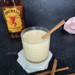 Fireball eggnog with a cinnamon stick and a bottle of fireball in the backround