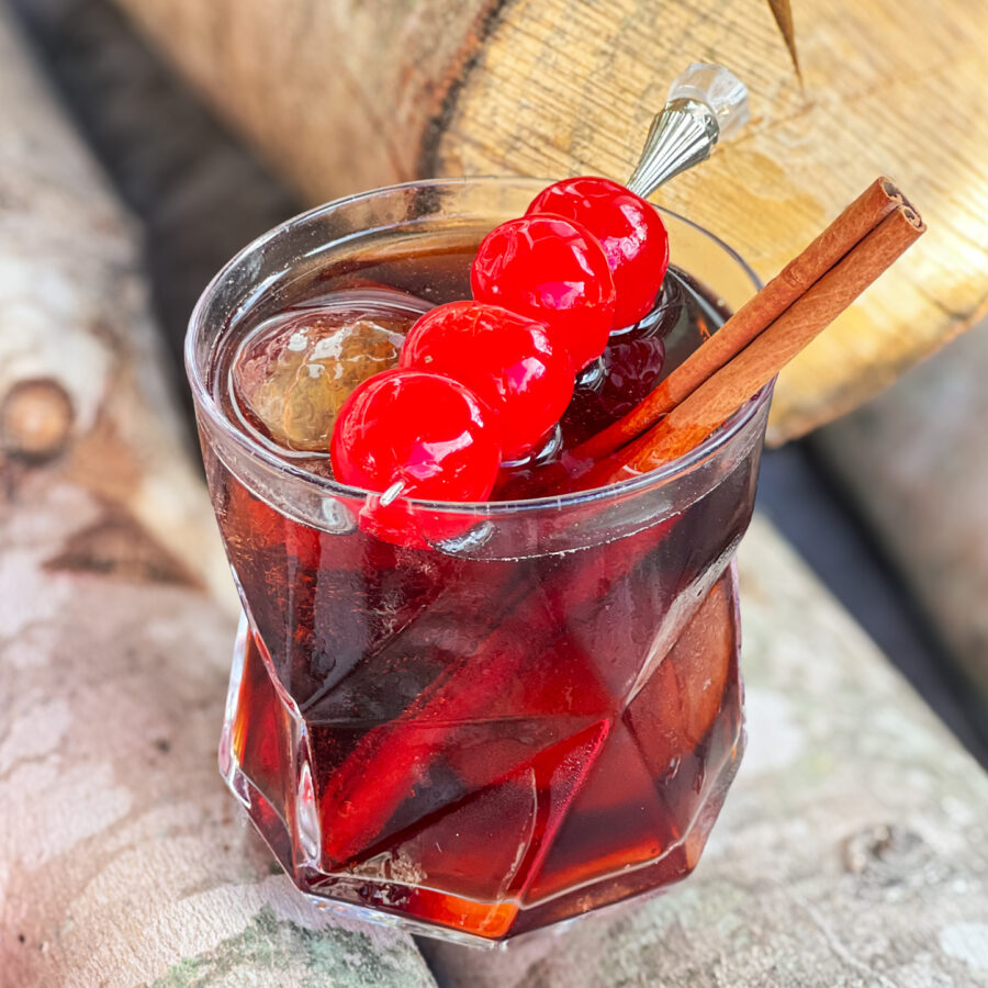 Dr. Pepper and Fireball with cherries as a garnish and a cinnamon stick in a glass on logs