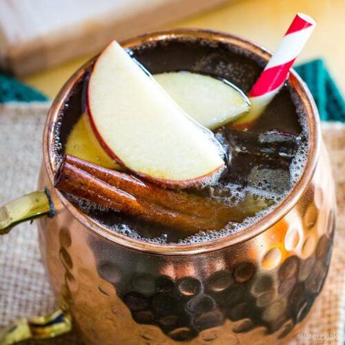 spiced apple cider moscow mule made with fireball in a copper mug with apples and a straw