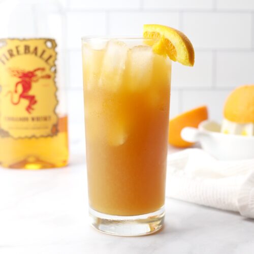 a tall glass of fireball orange sweet tea with a bottle of fireball and an orange squeezed