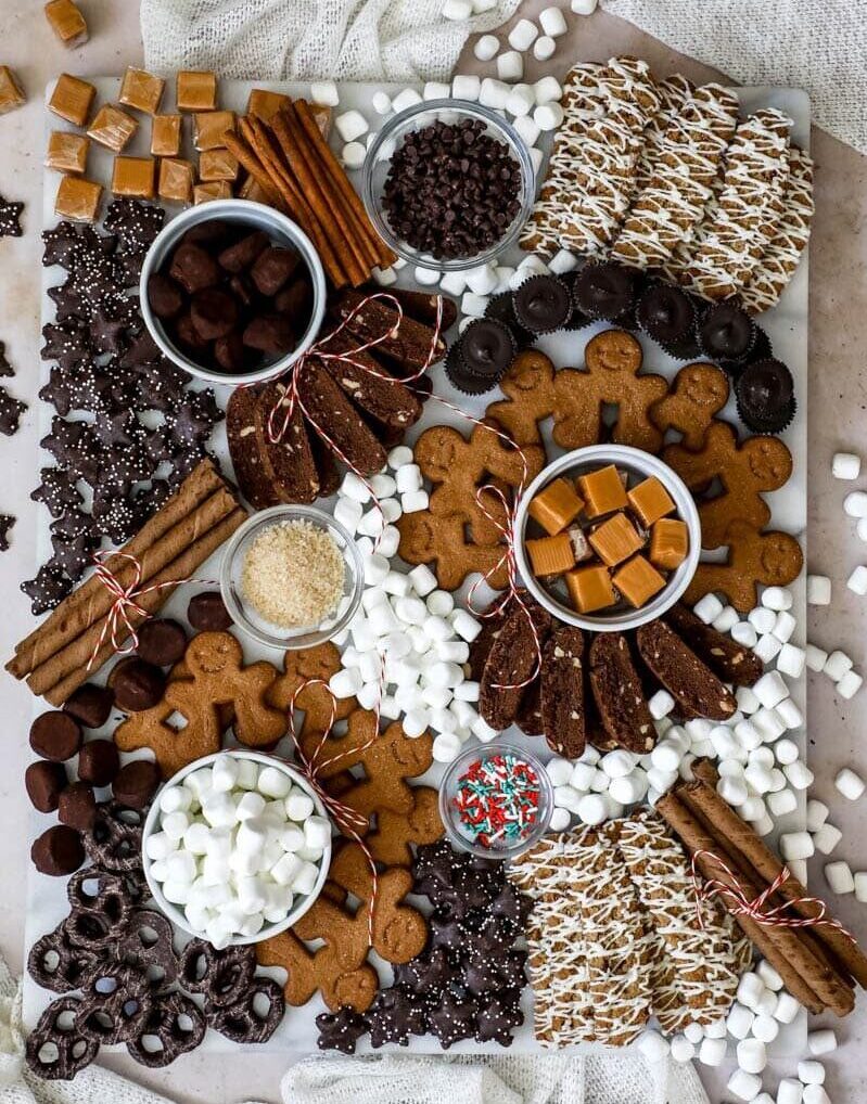 Hot chocolate holiday charcuterie boar idea with lots of toppings for hot chocolate like gingerbread and caramels and marshmallows