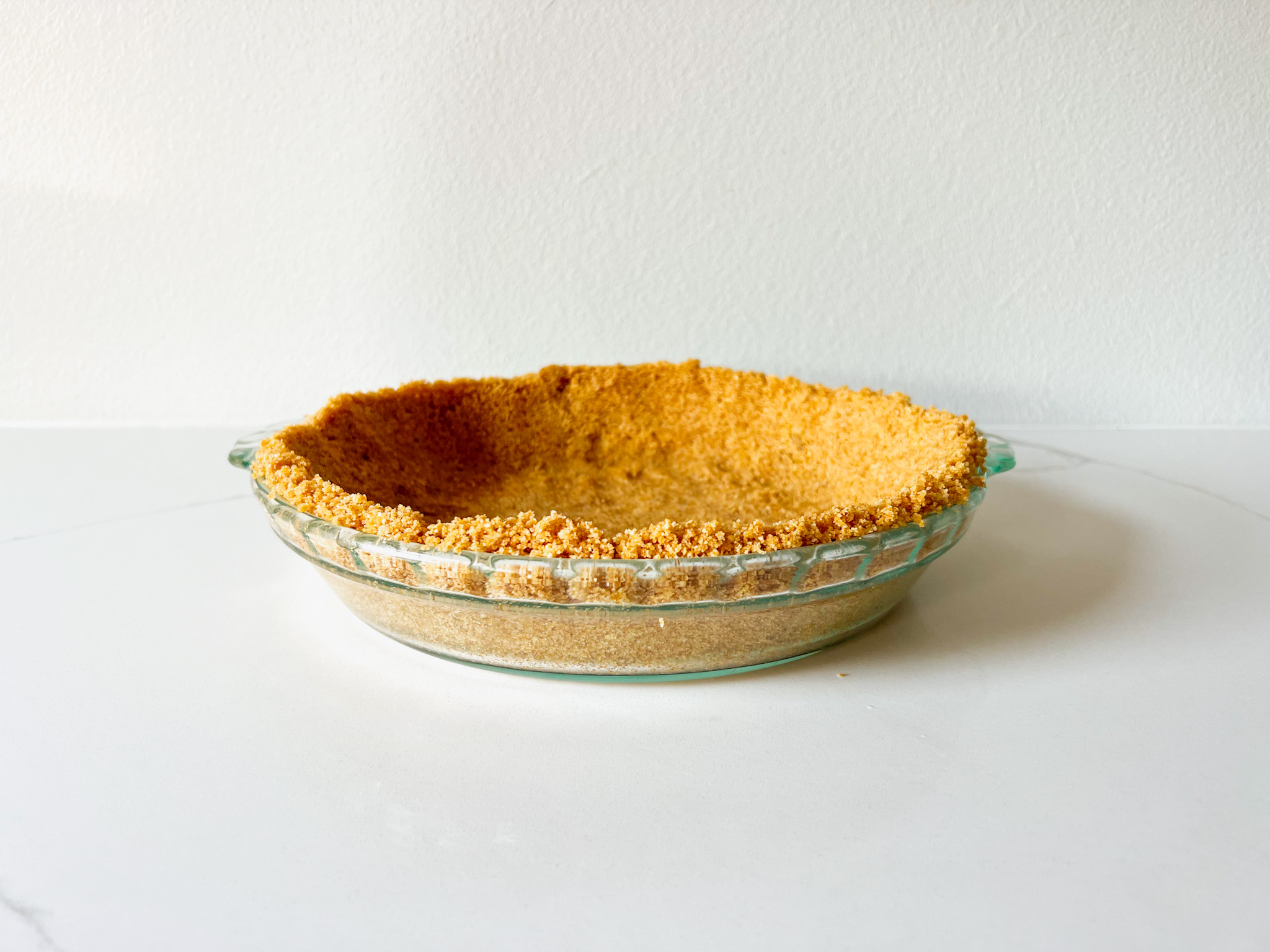Graham cracker crust in a pie dish on a white table