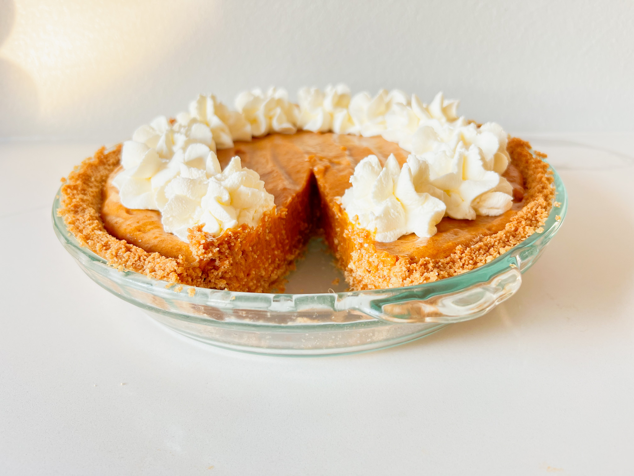 graham cracker crust pumpkin chiffon pie with whipped cream with a slice missing